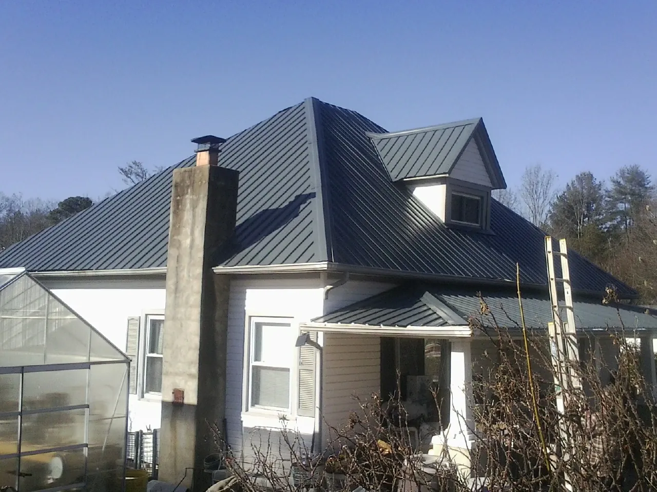 Dark blue standing seam metal roof on a white farmhouse with dormer — Slate & Tile Roof Repair by Roofing Brothers in Trimble
