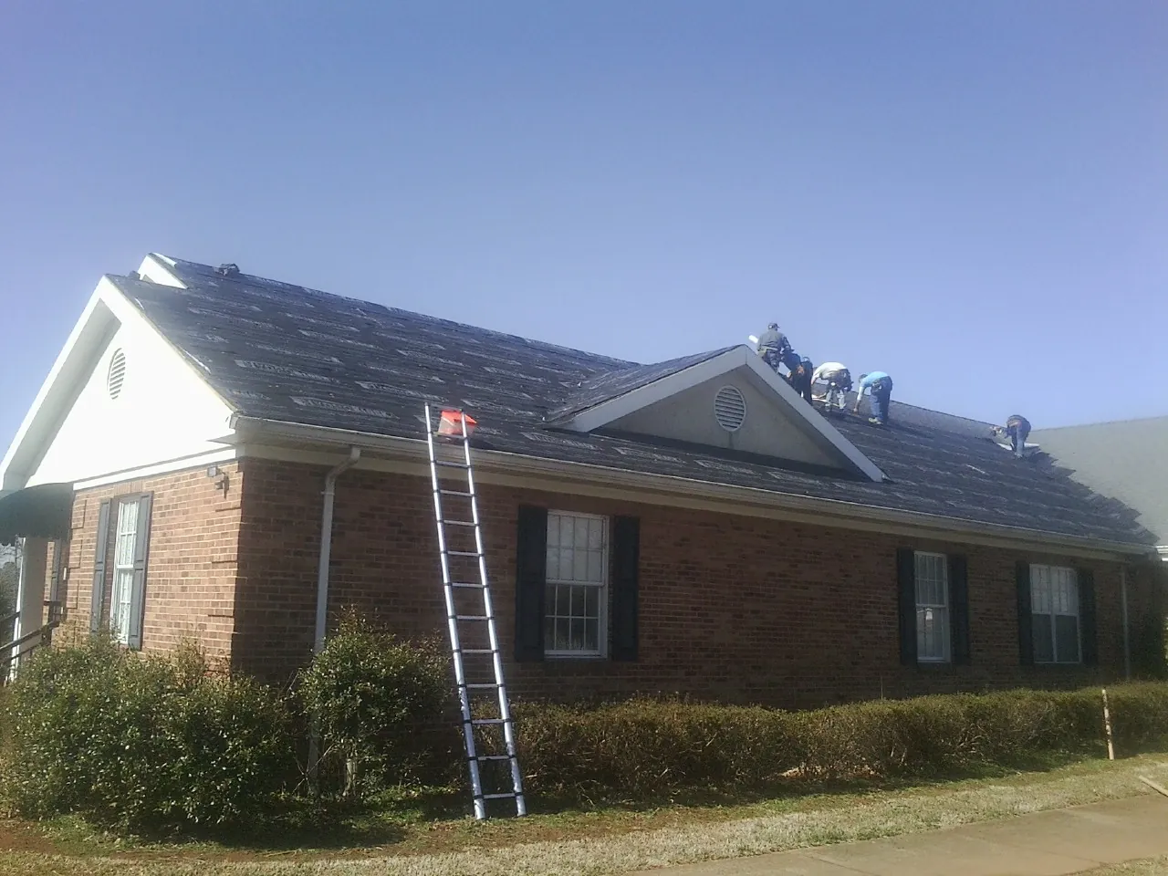 Crew tearing shingles off a brick ranch roof with a ladder set — Emergency Roof Repair work by our crew in Trimble