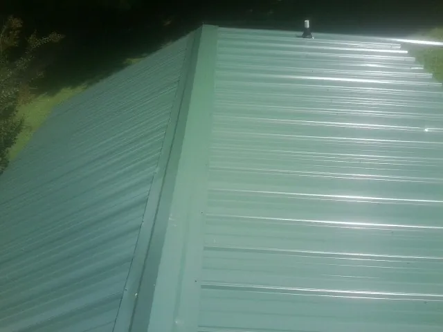 New green metal panels meeting at the ridge of a roof — Flat Roof Repair work by our crew in Trimble
