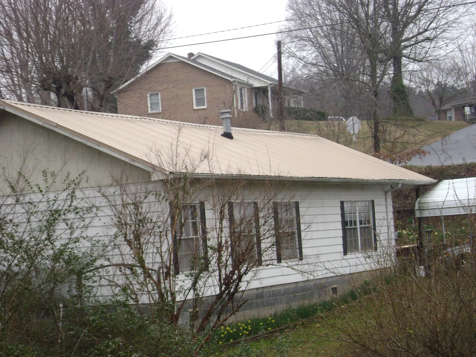 Tan metal roof on a white sided house set into a hillside — Commercial Roofing by Roofing Brothers in Trimble